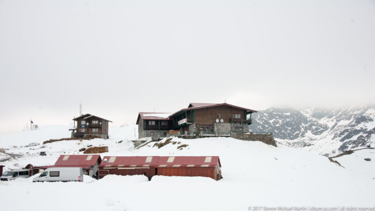 Cluster of mountain lodges and red-roofed buildings on deep snow with rugged peaks behind.