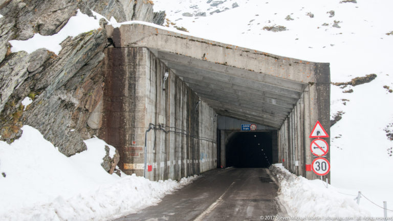 Concrete Bâlea Tunnel portal in a snowy rock face, with traffic signs and a 30 km/h speed limit.