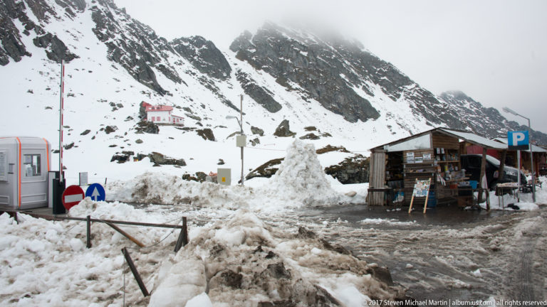 Snowy roadside visitor area with small buildings beneath steep Făgăraș mountain slopes.