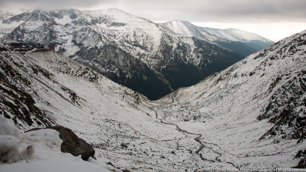 High view into a broad snowy mountain valley with a winding stream on the basin floor.