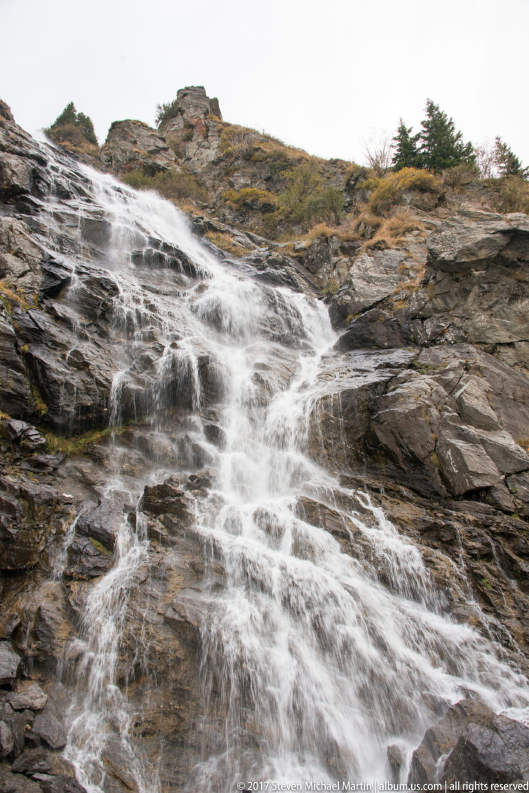 Broad white cascade spreading over dark stepped rock in the mountains.