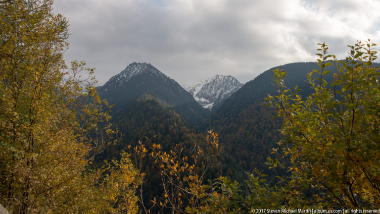 Snow-dusted Făgăraș peaks rising above dark forest and yellow autumn foliage.
