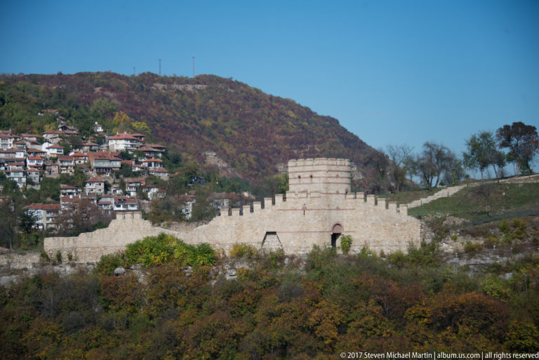 Pale crenellated fortress wall and tower below a densely built residential hillside.