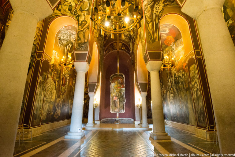 Interior of the Patriarchal Church on Tsarevets with pale columns, chandelier, and Teofan Sokerov’s monumental wall paintings.