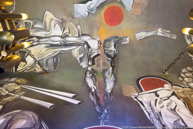 Teofan Sokerov mural detail with an inverted figure beneath a red disc, surrounded by limbs, chains, and angular gray forms.