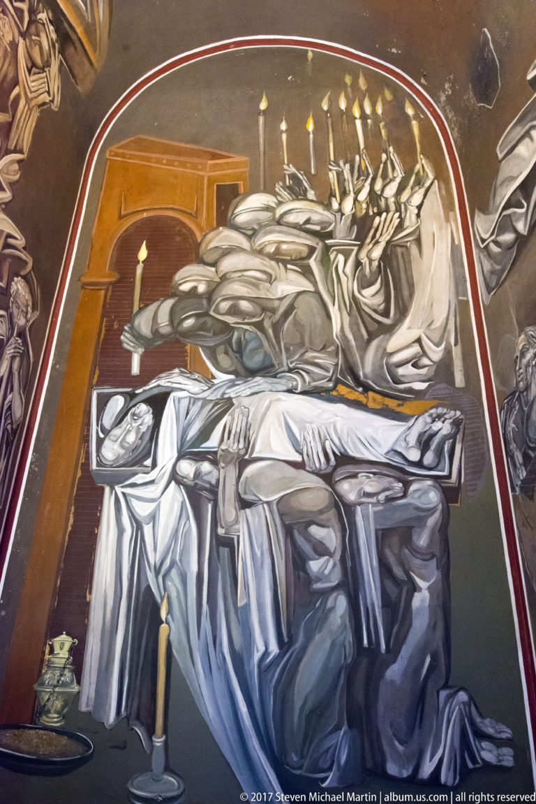 Teofan Sokerov mural with a pale reclining figure, clustered attendants, and a dense row of burning candles.