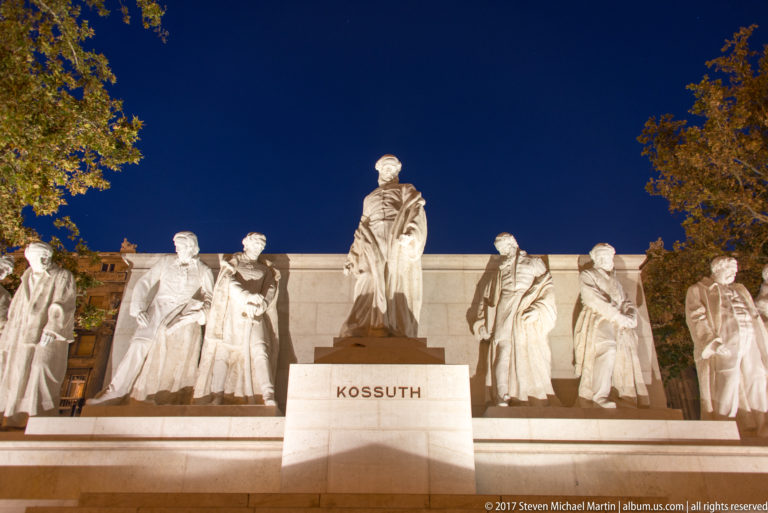 Illuminated Kossuth Memorial with the central statue of Lajos Kossuth and flanking figures against a dark sky.