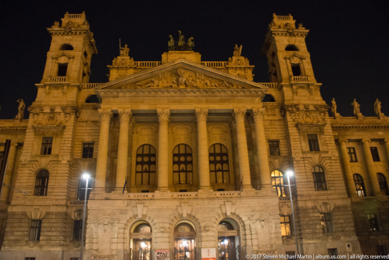 Illuminated former Palace of Justice with Corinthian columns, sculpted pediment, corner towers, and arched entrances.