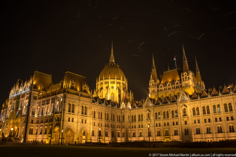Broad night view of the floodlit Hungarian Parliament, including its central dome and long ornate wings.