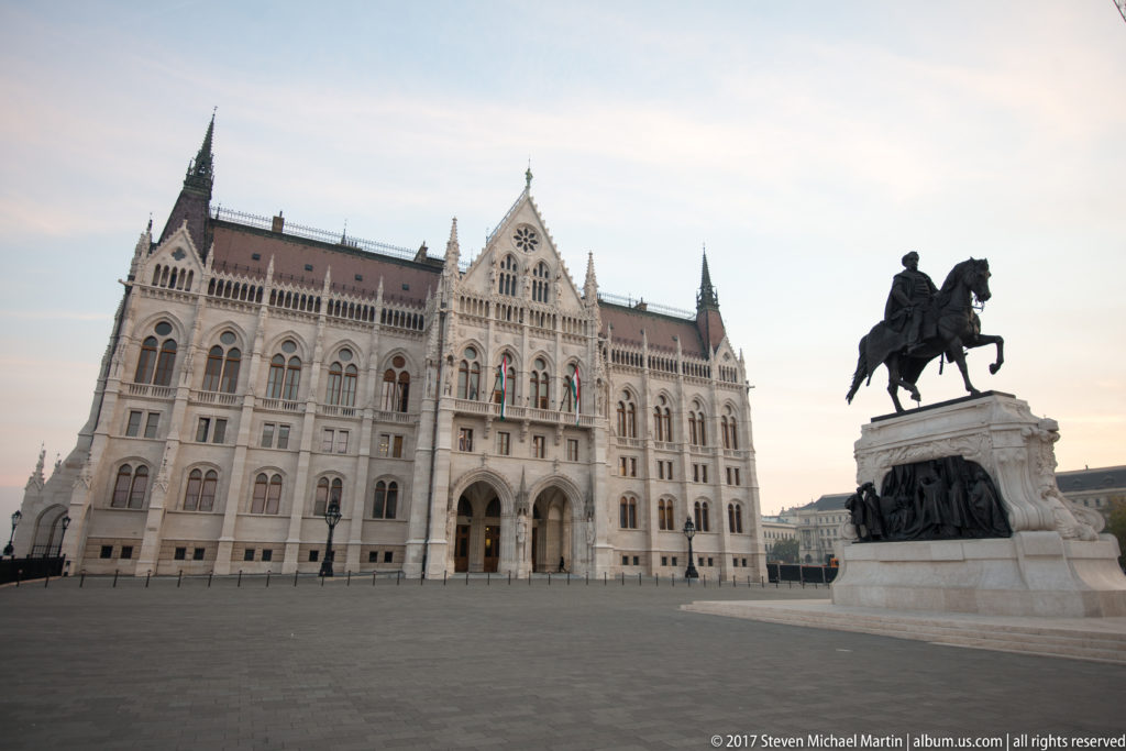 Hungarian Parliament in soft daylight with a bronze equestrian monument at right across Kossuth Lajos Square.