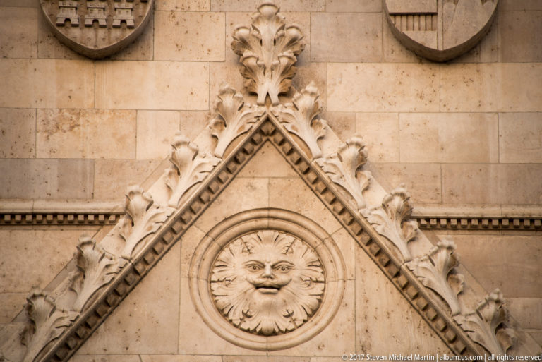Round carved face medallion framed by leafy ornament and pointed molding in a Parliament gable.