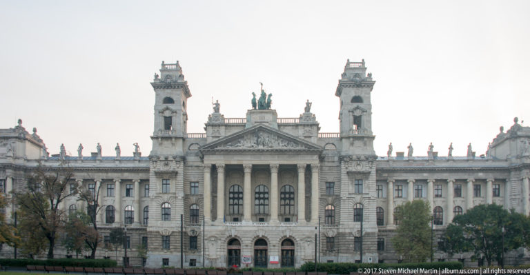 Frontal daylight view of the former Palace of Justice with central columns, pediment, rooftop statues, and tall corner towers.