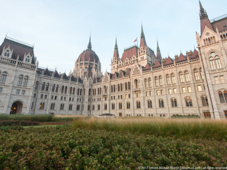 Hungarian Parliament and central dome rising beyond low ornamental grasses and shrubs in the foreground.