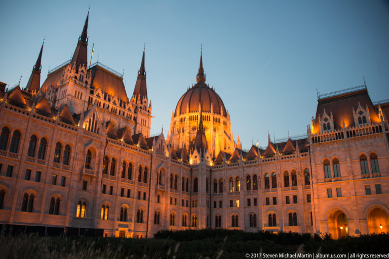 Illuminated Hungarian Parliament at blue hour, with its dome, steep roofs, pinnacles, and ornate façades.