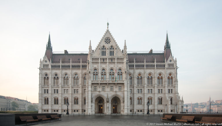 Symmetrical Parliament end façade with twin spires, rose window, tall Gothic openings, and paired entrance arches.