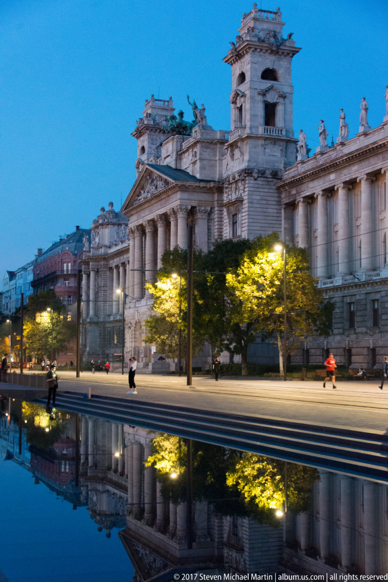 Illuminated former Palace of Justice with classical columns and towers reflected in water at Kossuth Lajos Square.