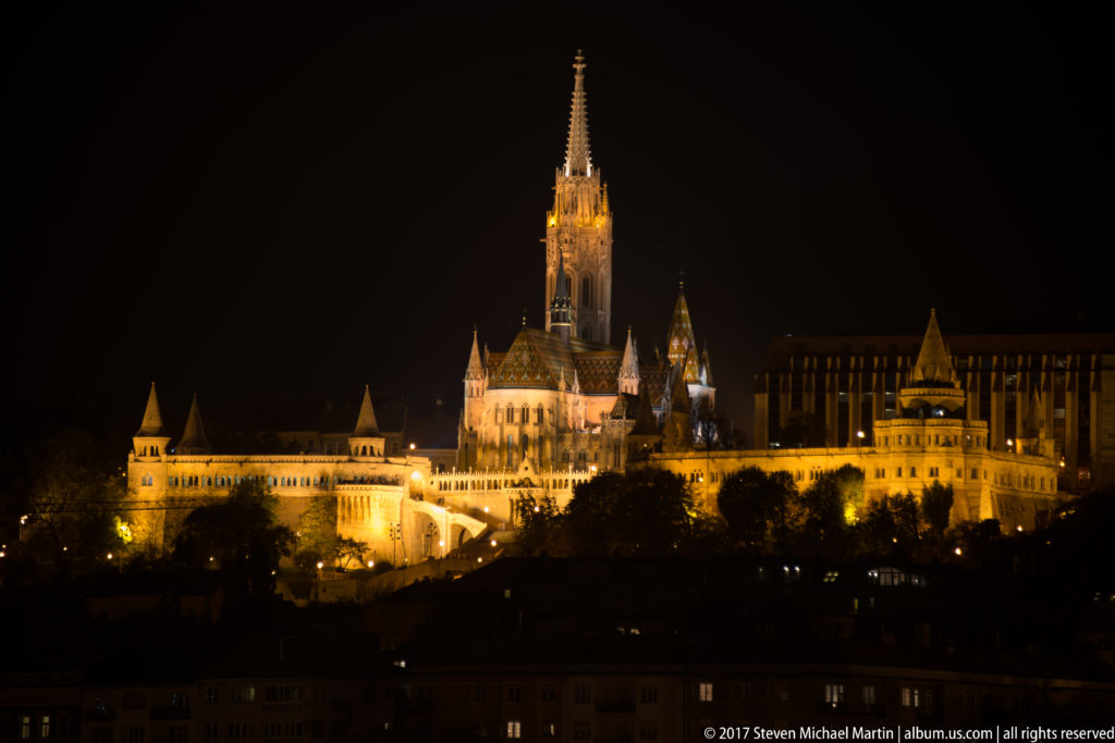 Floodlit Matthias Church rises above the illuminated arcades and turrets of Fisherman’s Bastion at night on Castle Hill.