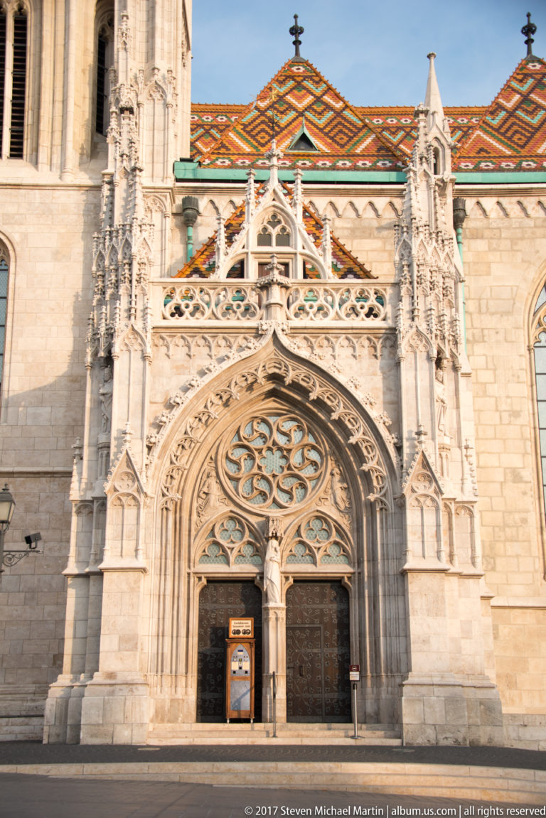 Ornate pointed south portal of Matthias Church with carved tracery, pinnacles, and patterned tile roof above.