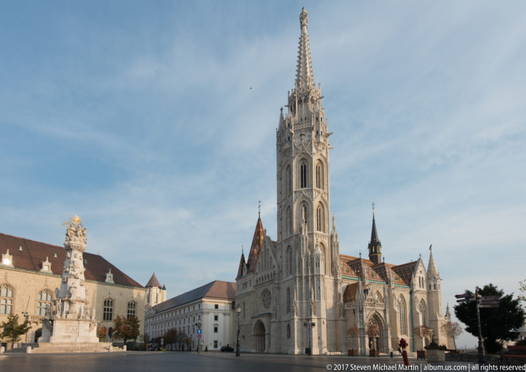 Matthias Church with its tall spire and patterned roof beside the Holy Trinity Column in Budapest’s Castle District.