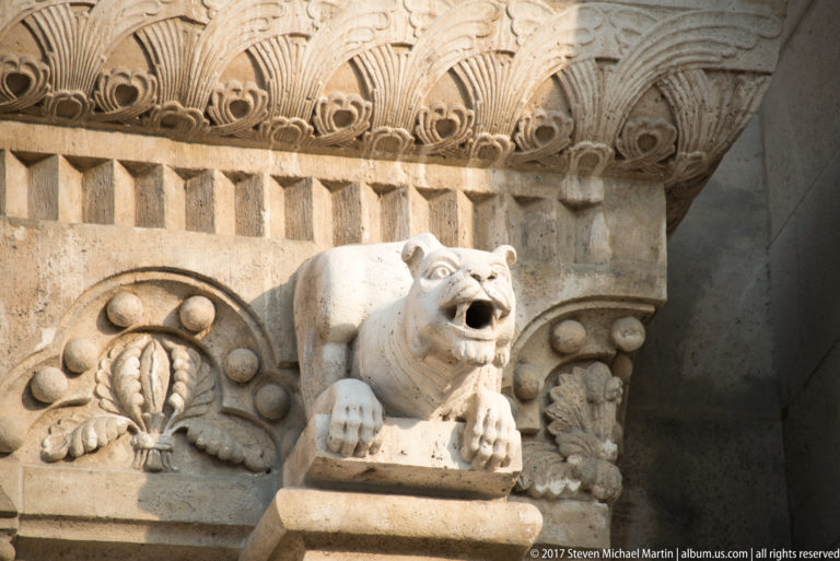 Bear-like carved stone animal projecting from an ornamented wall with foliate relief and patterned cornice near Fisherman’s Bastion.