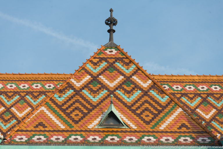Close view of Matthias Church’s multicolored geometric glazed-tile roof with a small triangular opening and ridge finial.