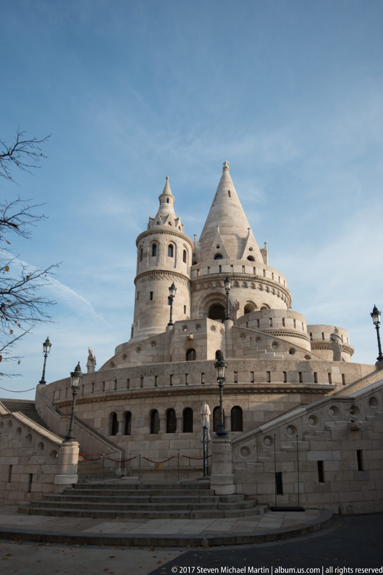 Broad stair and balustrade leading to clustered conical towers of Fisherman’s Bastion under a blue sky.