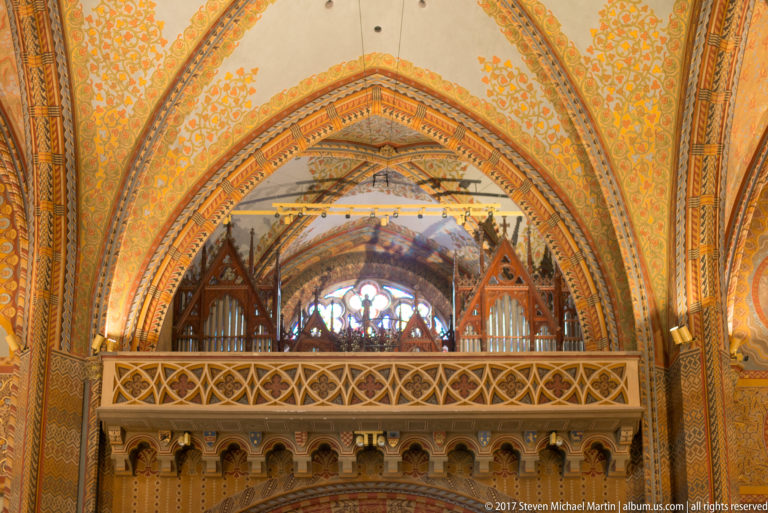 Decorated pointed arch and wooden organ loft inside Matthias Church, with organ pipes and painted vault surfaces.
