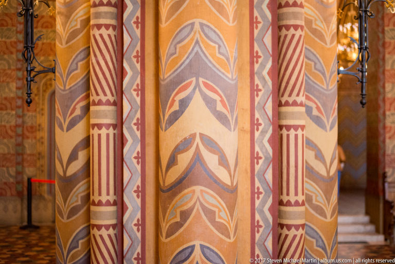 Close view of painted church columns with red, cream, gray, and blue geometric and foliate patterns.