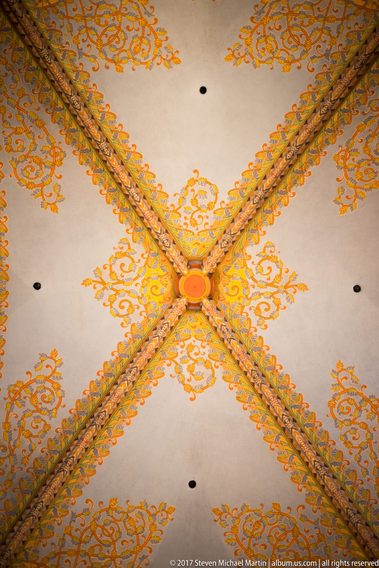 Symmetrical upward view of a ribbed vault bay with central boss and orange foliate decoration on pale ceiling fields.