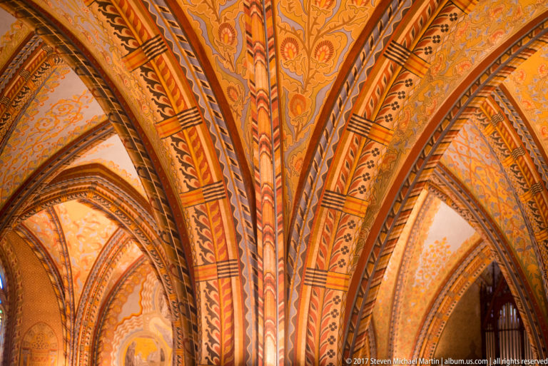 Upward view of clustered painted ribs branching into pointed arches beneath ornate vaults in Matthias Church.