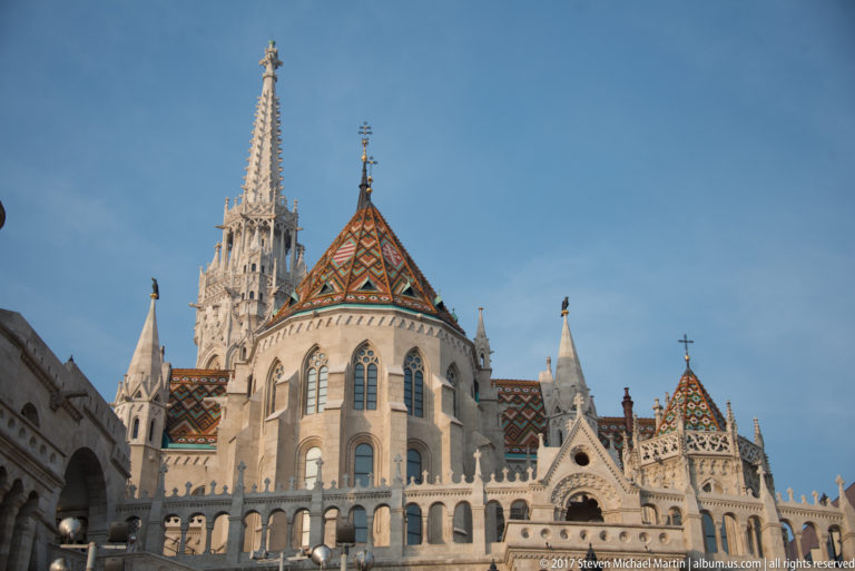 Matthias Church east end with lancet windows, colorful patterned roof, pinnacles, and tall Gothic Revival spire above the bastion.