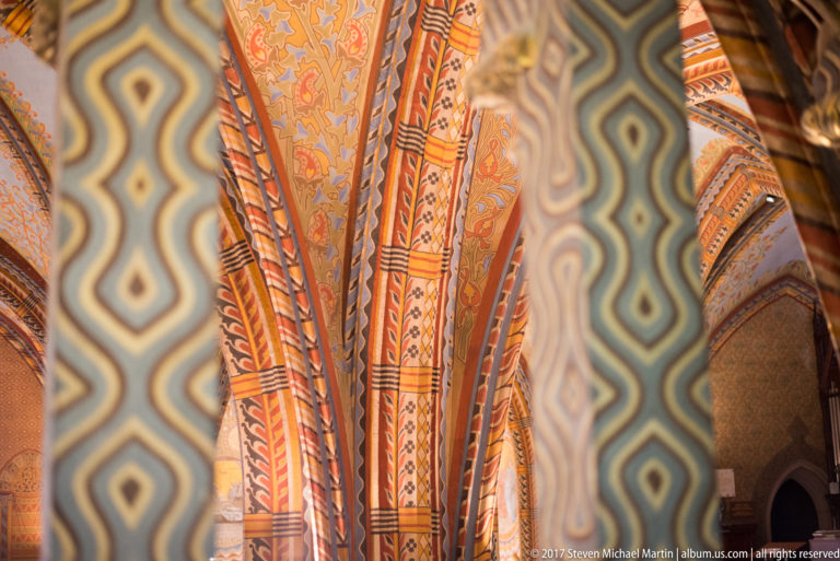 Painted ribs and vaults seen behind an out-of-focus foreground screen with repeating wavy geometric patterns.