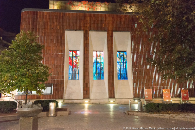 Night view of the Wyspiański Pavilion 2000 in Krakow, with a brick façade and three tall illuminated stained-glass windows.