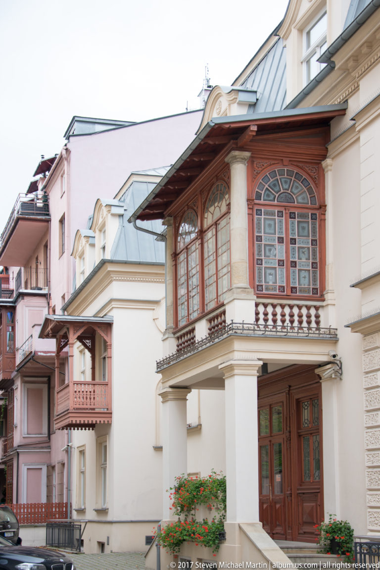 Historic Kraków townhouse with an ornate enclosed wooden bay, carved details, and neighboring pastel façades.