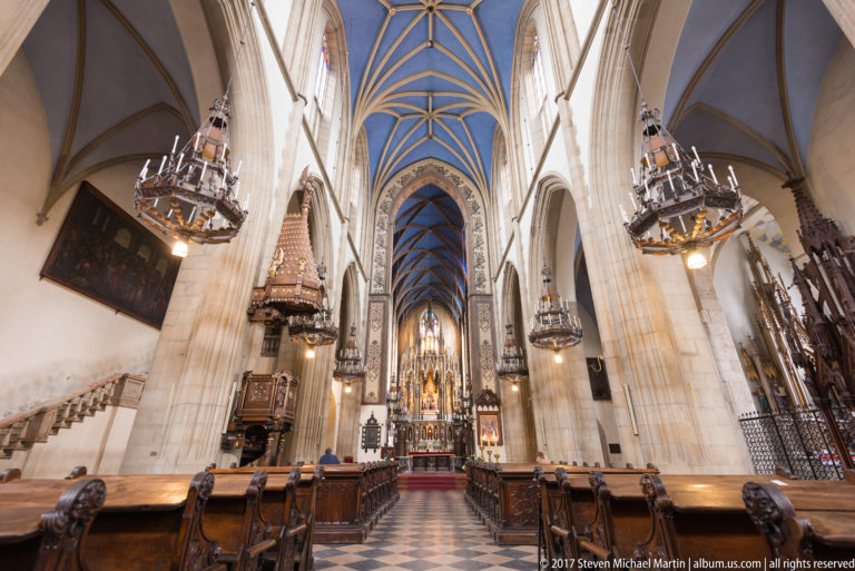 Gothic church chancel in Kraków with dark choir furnishings, blue rib vaults, chandeliers, and a richly carved high altar.