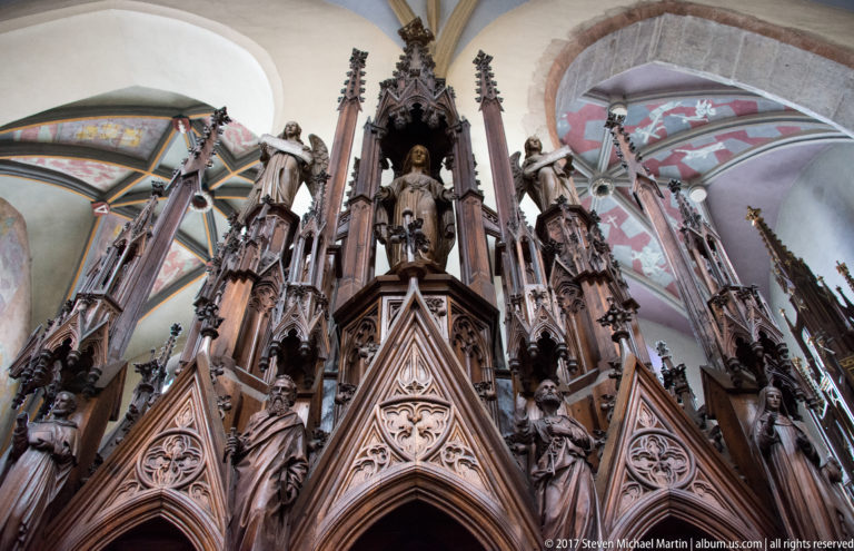 Elaborate Gothic carved church canopy or screen in Kraków, with pointed arches, pinnacles, tracery, and standing saint figures.