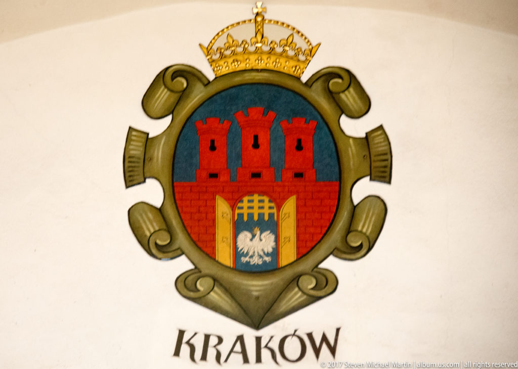 Kraków coat of arms with crown, red three-towered city walls, open gate, white Polish eagle, and the word KRAKÓW below.