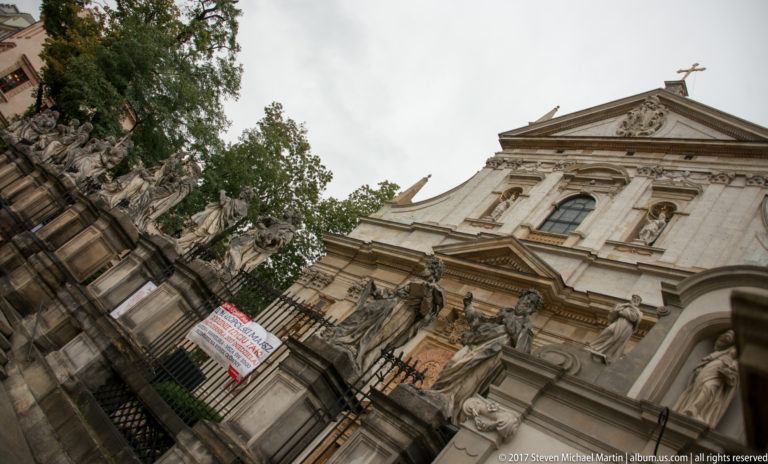 Upward view of the Church of Saints Peter and Paul in Kraków, with Baroque façade and stone apostle statues along the forecourt.