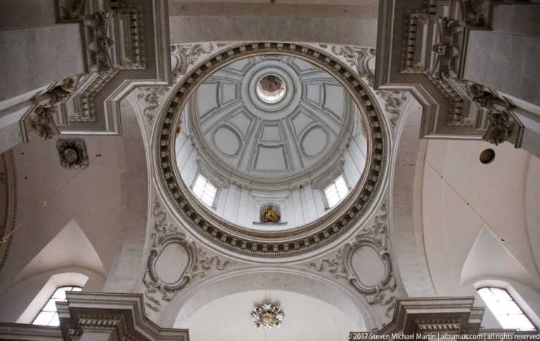Upward view into a pale coffered church dome in Kraków, with windowed drum, molded ornament, and supporting arches.