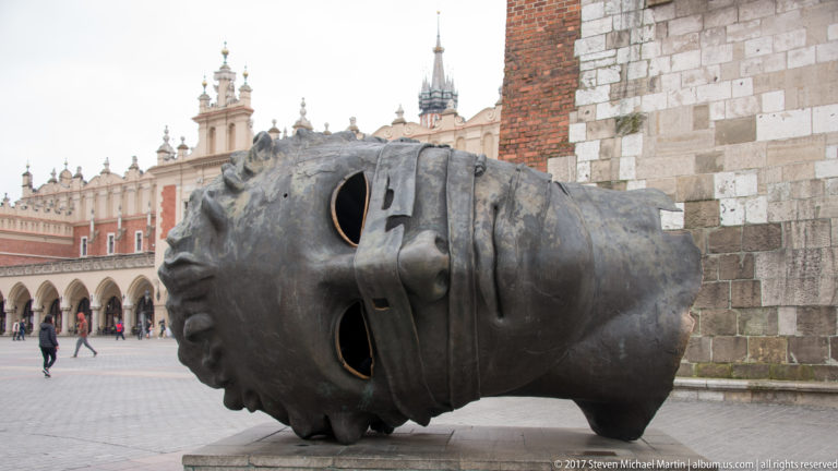 Igor Mitoraj’s large bronze Eros Bendato head lying horizontally on Kraków’s Main Market Square.