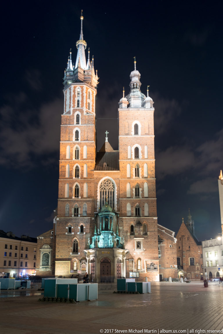 Front night view of St. Mary’s Basilica in Krakow, showing its two unequal brick towers and Gothic central window.