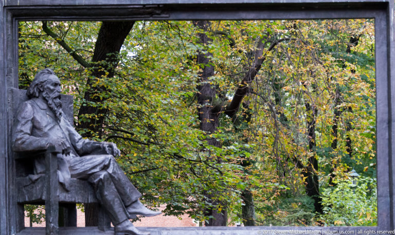 Bronze statue of a bearded seated man holding an open book in a leafy Kraków park.