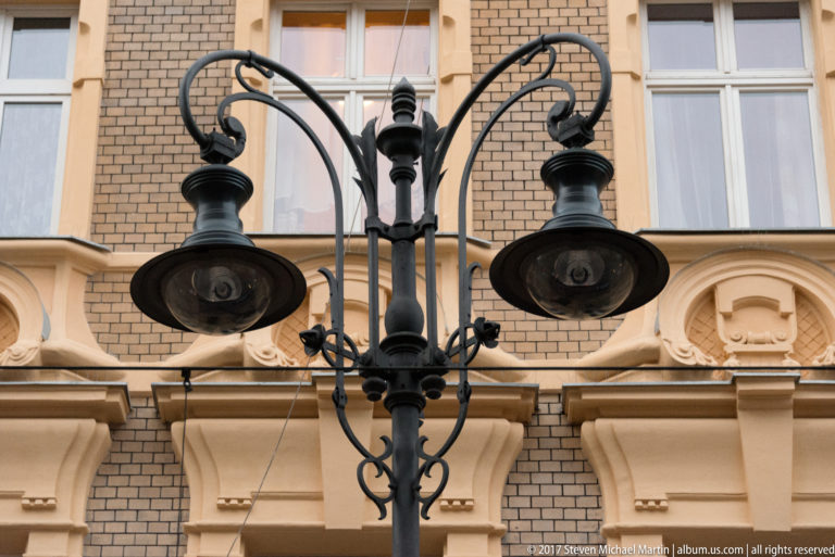 Ornamental black double-headed street lamp with curved arms and round shades against a detailed historic Kraków façade.