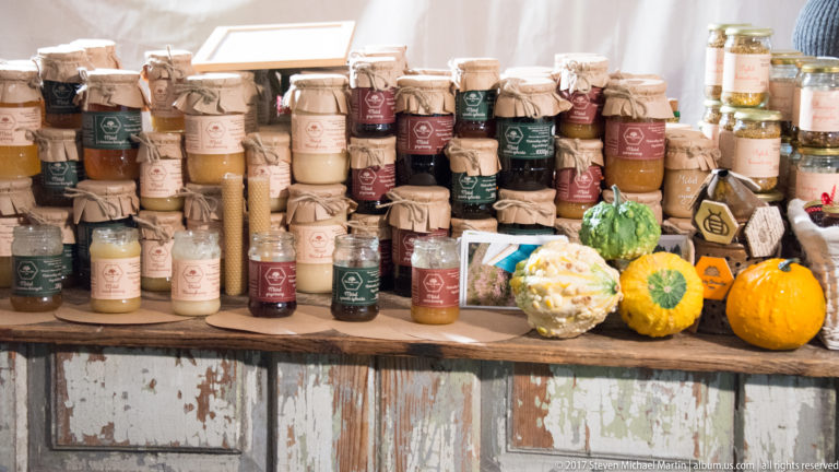 Rustic Kraków market display of cloth-capped jars of preserves and condiments arranged with small autumn squash and produce.