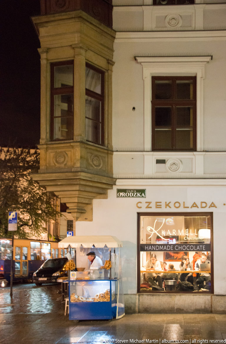 Karmello handmade chocolate storefront on a wet Kraków street, with bright display window, outdoor counter, and CZEKOLADA sign.