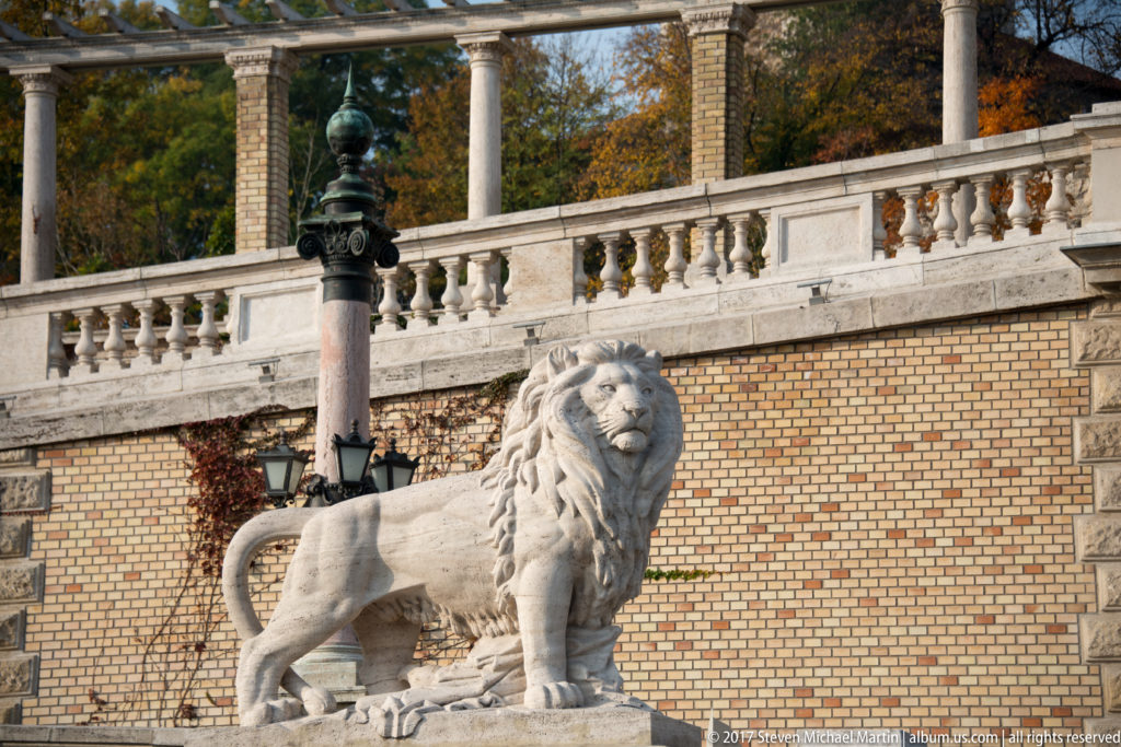 Seated stone lion before a balustrade and yellow-brick terrace wall at the Castle Garden Bazaar.