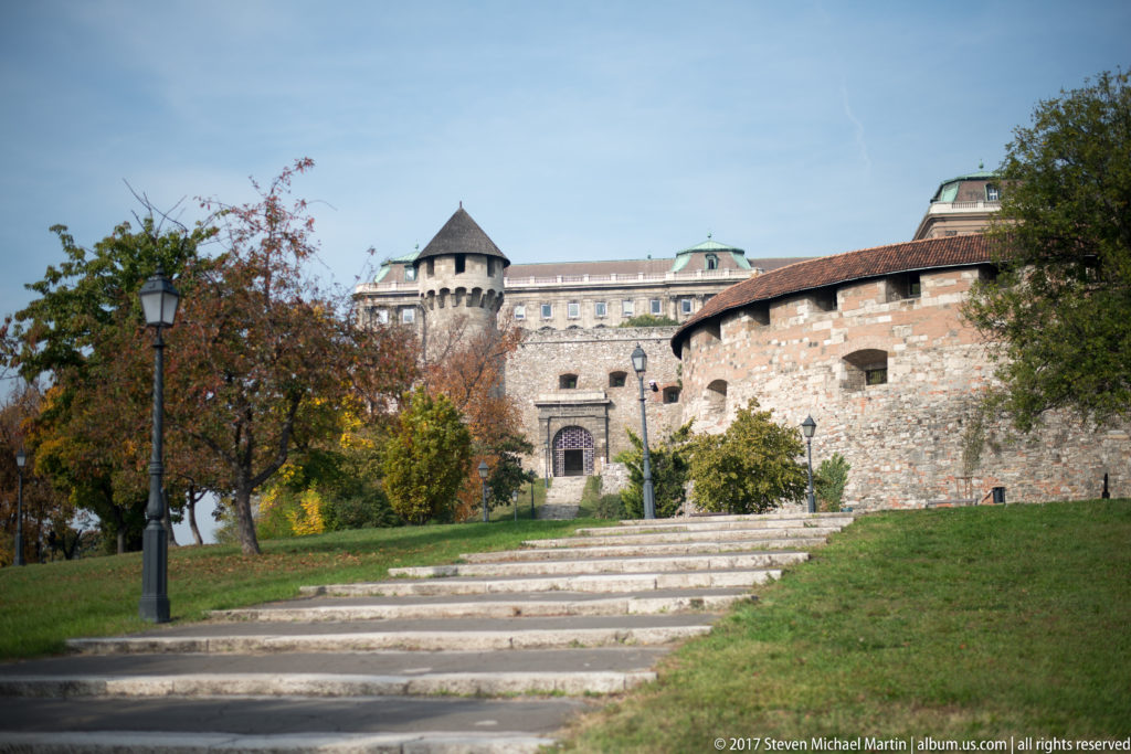 Path approaching mixed-stone Castle Hill fortifications with a rounded wall projection and small roofed tower.
