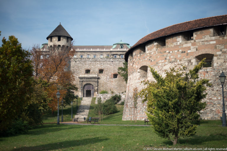 Rounded masonry fortification wall with mixed stonework, a roofed tower, and recessed doorway on Castle Hill.