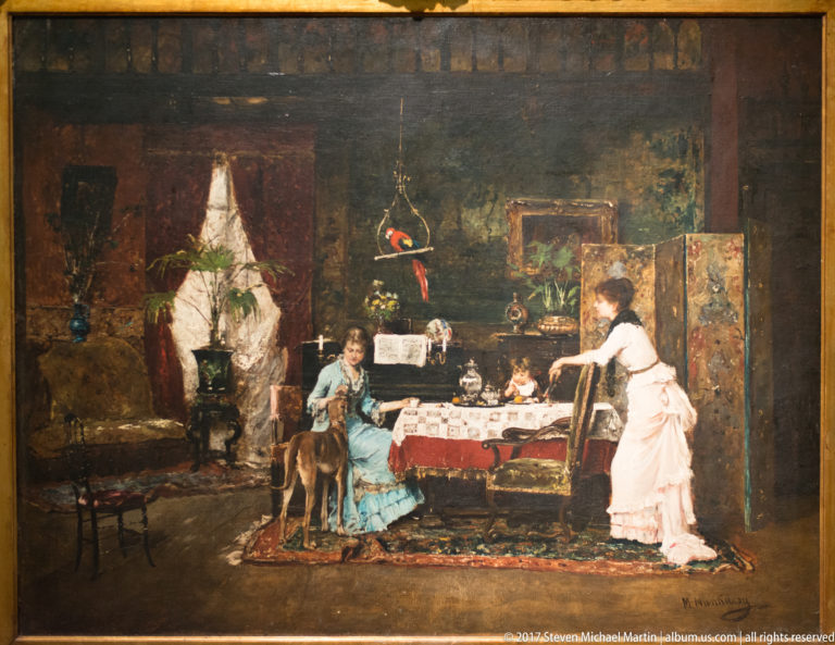 Genre painting of women and a child gathered around a table in a richly furnished domestic interior.