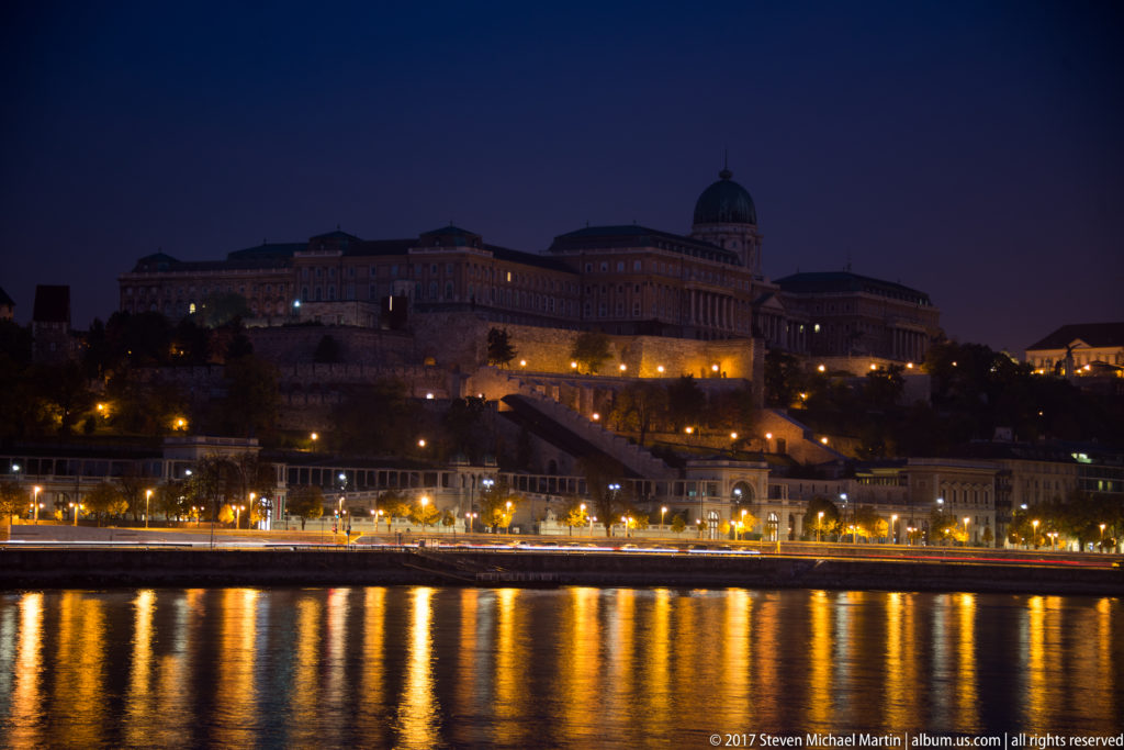 Illuminated Buda Castle and Royal Palace at night, with golden reflections on the Danube.